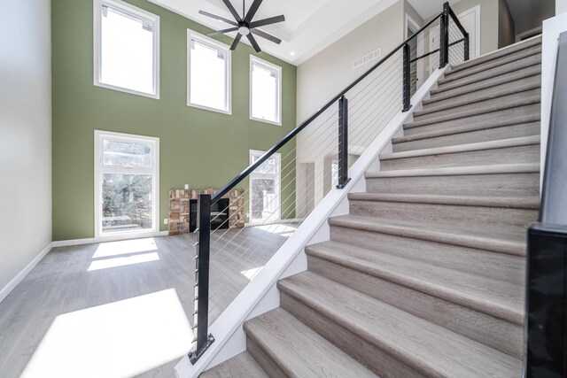 stairway featuring a high ceiling, wood finished floors, visible vents, a ceiling fan, and baseboards