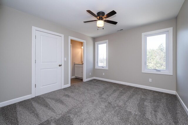 unfurnished bedroom featuring dark colored carpet, multiple windows, and visible vents