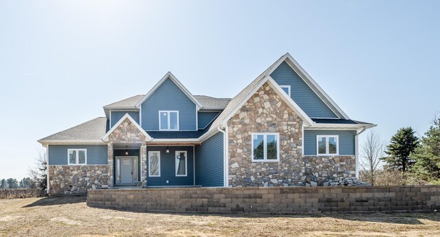 craftsman-style home featuring stone siding, a shingled roof, and covered porch