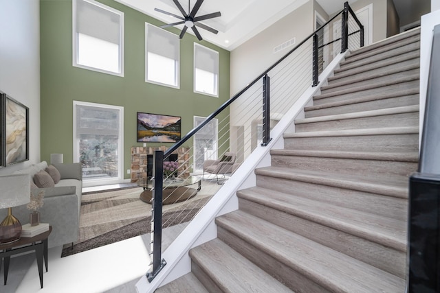 stairs with wood finished floors, visible vents, a high ceiling, and ceiling fan