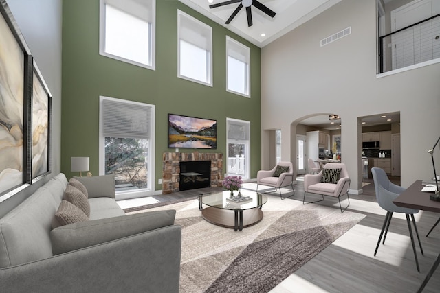 living area with wood finished floors, visible vents, a ceiling fan, arched walkways, and high vaulted ceiling