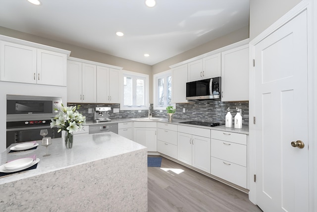 kitchen with stainless steel microwave, decorative backsplash, white cabinetry, and a sink