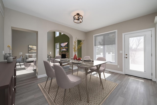 dining area featuring arched walkways, dark wood finished floors, a fireplace, and baseboards