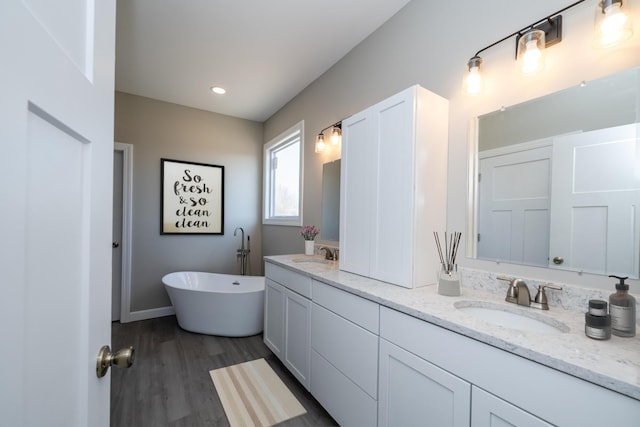 full bath featuring a freestanding bath, wood finished floors, a sink, and double vanity