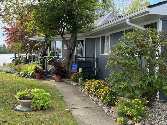 view of exterior entry featuring a lawn and a shingled roof