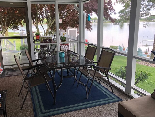 sunroom featuring carpet flooring, outdoor dining area, and a water view