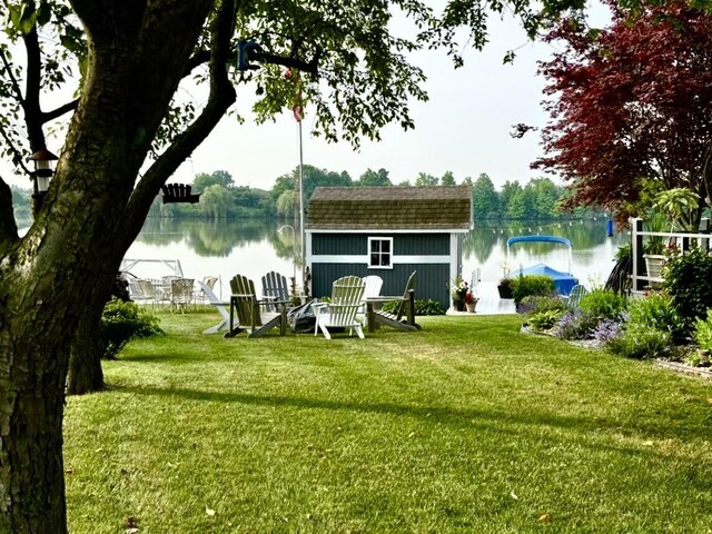 rear view of house featuring a water view, a storage unit, an outdoor structure, and a yard