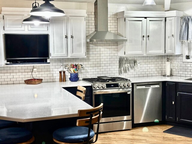 kitchen featuring wall chimney exhaust hood, light countertops, stainless steel appliances, and light wood-type flooring