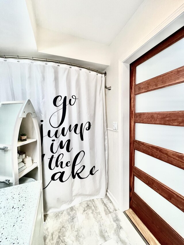 full bathroom with marble finish floor, a shower with shower curtain, and wainscoting