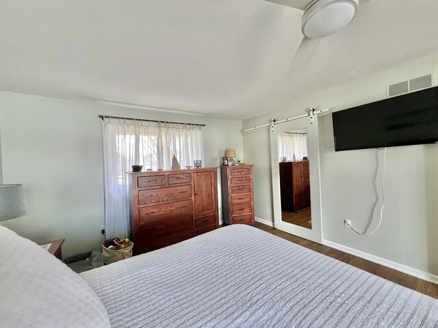 bedroom featuring baseboards, visible vents, a barn door, and wood finished floors