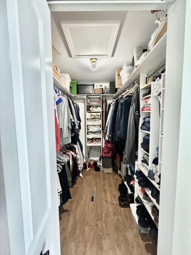 walk in closet with attic access and wood finished floors