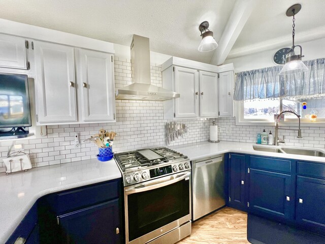 kitchen featuring blue cabinetry, light countertops, a sink, appliances with stainless steel finishes, and wall chimney exhaust hood