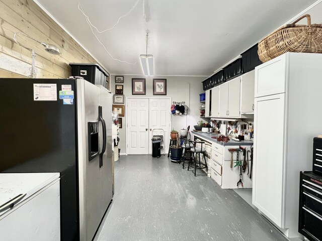 kitchen featuring white cabinetry, wood walls, stainless steel fridge, and concrete flooring