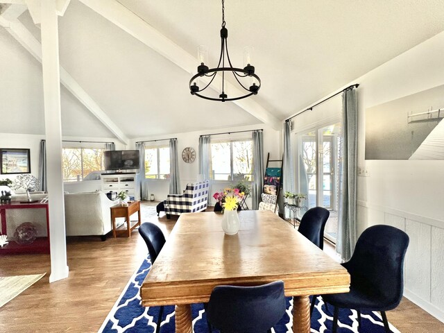 dining space with a wainscoted wall, lofted ceiling with beams, light wood-style floors, and a chandelier