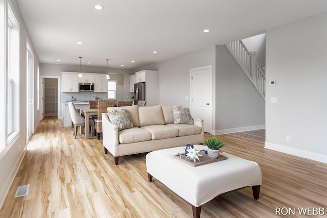 living room featuring visible vents, light wood finished floors, baseboards, stairs, and recessed lighting