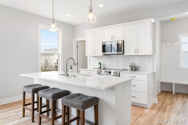 kitchen featuring a kitchen island with sink, a sink, stainless steel appliances, and tasteful backsplash