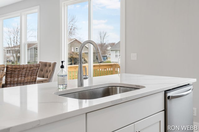 interior details with white cabinetry, a sink, light stone counters, and stainless steel dishwasher