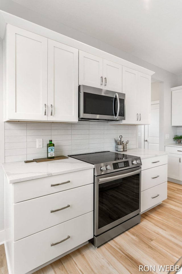 kitchen with light stone countertops, appliances with stainless steel finishes, white cabinets, light wood-style floors, and decorative backsplash