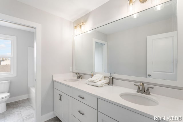 full bathroom featuring toilet, a sink, double vanity, and baseboards
