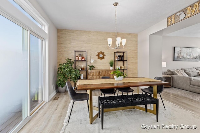 dining area with a chandelier, light wood finished floors, and an accent wall