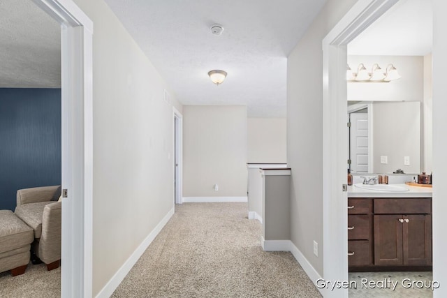 hallway featuring a sink, light carpet, and baseboards