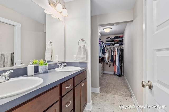 full bathroom with a walk in closet, double vanity, and baseboards