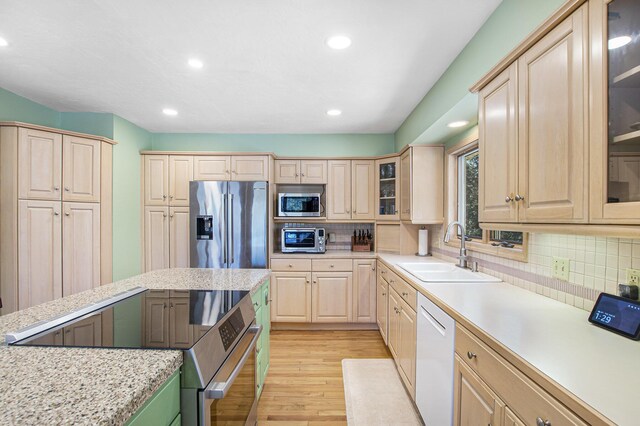 kitchen featuring a sink, light wood finished floors, light brown cabinetry, stainless steel appliances, and decorative backsplash