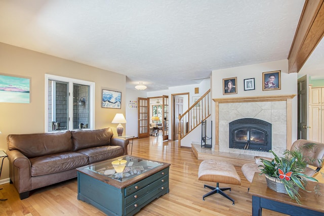 living room featuring light wood-style flooring, stairway, a premium fireplace, and a textured ceiling
