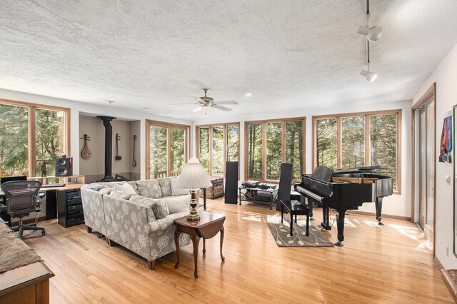 living area with a wood stove, a textured ceiling, light wood-type flooring, ceiling fan, and track lighting
