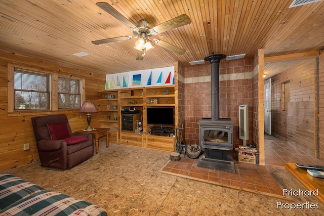 living room featuring wood ceiling, wood walls, a wood stove, and a ceiling fan