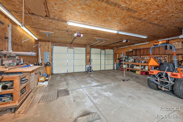 garage with a workshop area, a garage door opener, and electric panel