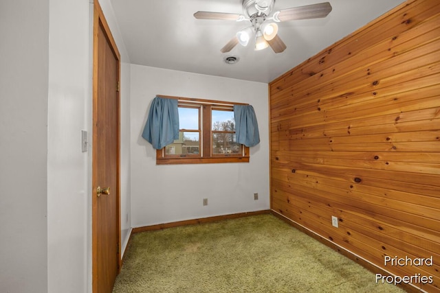 unfurnished bedroom featuring carpet floors, wood walls, baseboards, and ceiling fan