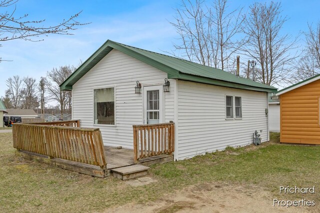 rear view of house with a lawn, an outbuilding, metal roof, and a deck