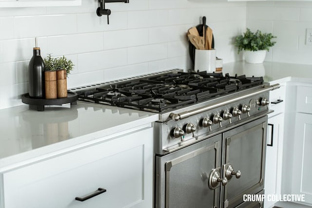 interior details featuring decorative backsplash, white cabinets, light countertops, and range with two ovens