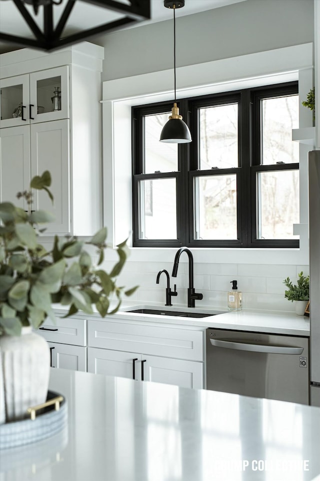 kitchen featuring light countertops, a sink, stainless steel dishwasher, glass insert cabinets, and white cabinets