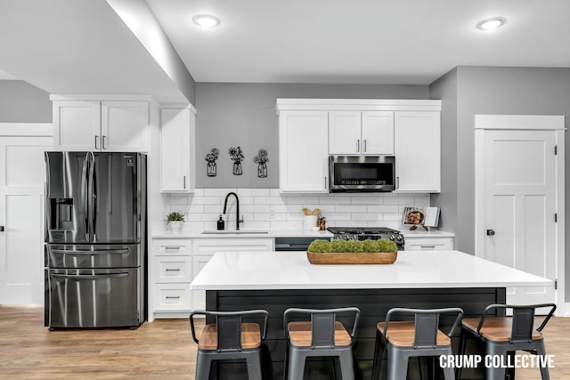 kitchen featuring black fridge with ice dispenser, light countertops, a breakfast bar, stainless steel microwave, and a sink