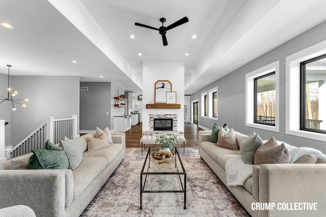 living area with recessed lighting, ceiling fan with notable chandelier, visible vents, a glass covered fireplace, and wood finished floors