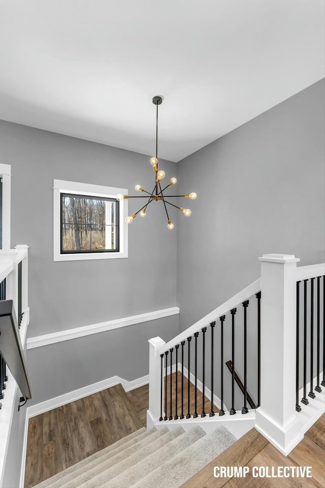 staircase with baseboards, wood finished floors, and a notable chandelier
