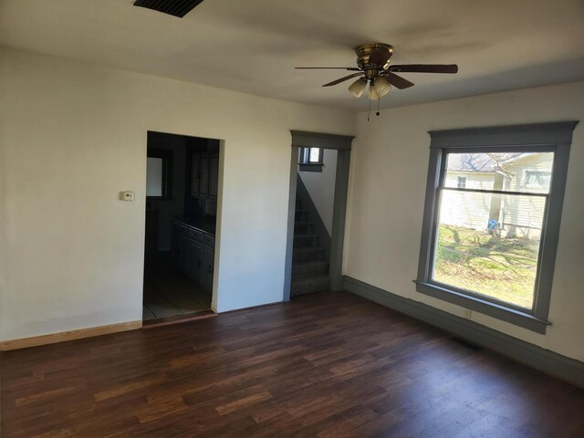 unfurnished room featuring stairs, ceiling fan, baseboards, and dark wood-type flooring
