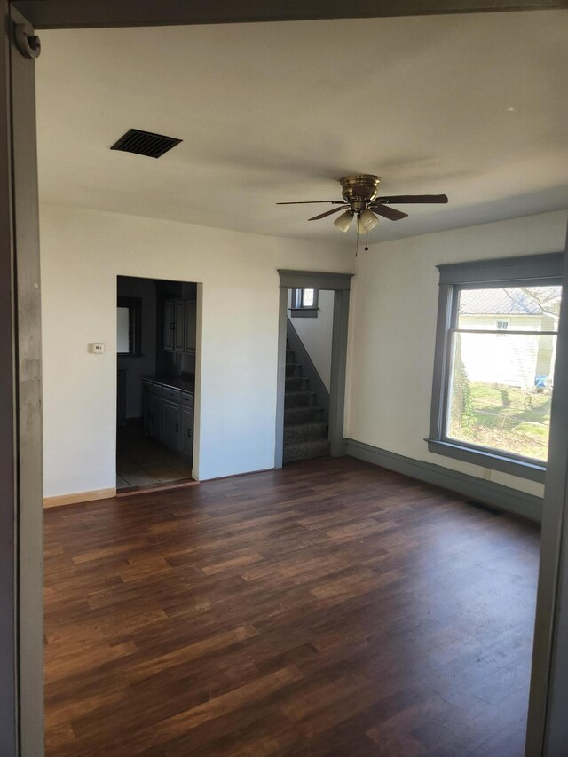 spare room with stairway, visible vents, ceiling fan, baseboards, and dark wood-style flooring