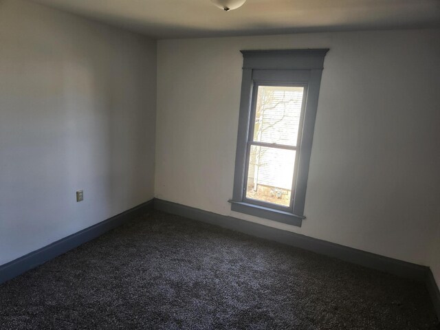 spare room with dark carpet and baseboards