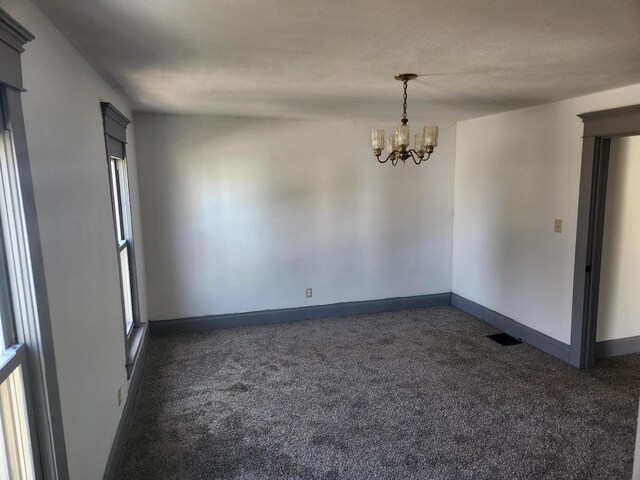 unfurnished room featuring dark carpet, an inviting chandelier, visible vents, and baseboards