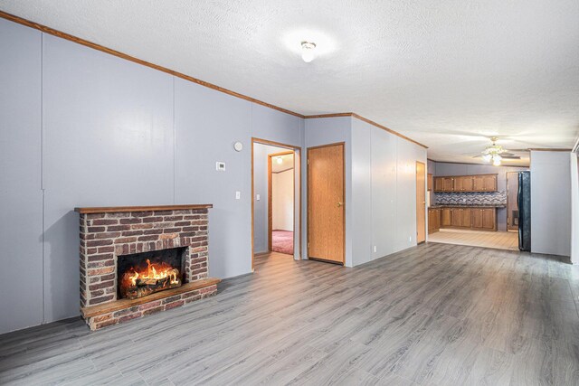 67173 Bulhand Rd, Cassopolis, MI 49031 - unfurnished living room with a brick fireplace, ornamental molding, a ceiling fan, a textured ceiling, and light wood-style floors