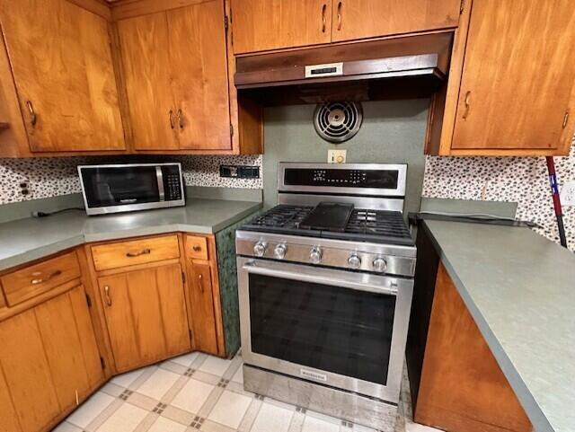 kitchen with brown cabinets, stainless steel appliances, under cabinet range hood, and light floors