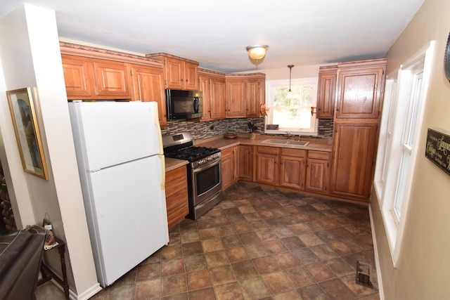 kitchen featuring black microwave, a sink, stainless steel range with gas stovetop, freestanding refrigerator, and decorative backsplash