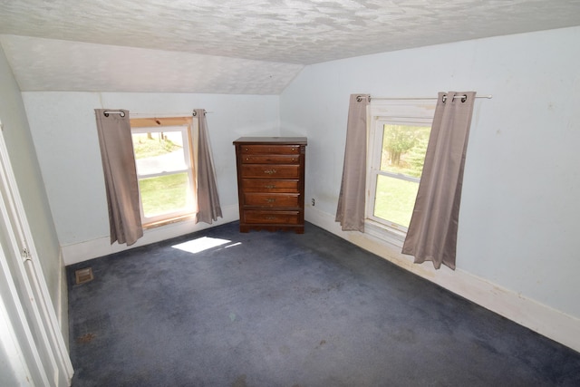 unfurnished bedroom featuring a textured ceiling, multiple windows, lofted ceiling, and dark colored carpet