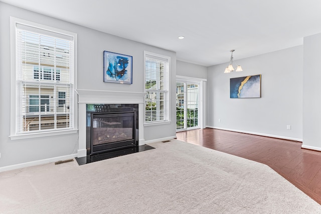 living area featuring a fireplace with flush hearth, visible vents, baseboards, carpet floors, and an inviting chandelier
