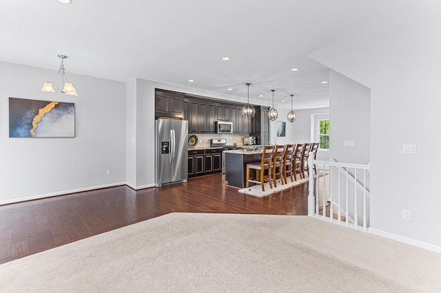 kitchen with a breakfast bar area, recessed lighting, dark wood-style flooring, stainless steel appliances, and hanging light fixtures