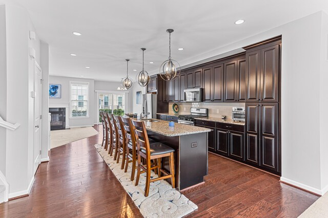 kitchen featuring an island with sink, backsplash, a breakfast bar, dark wood-style floors, and stainless steel appliances