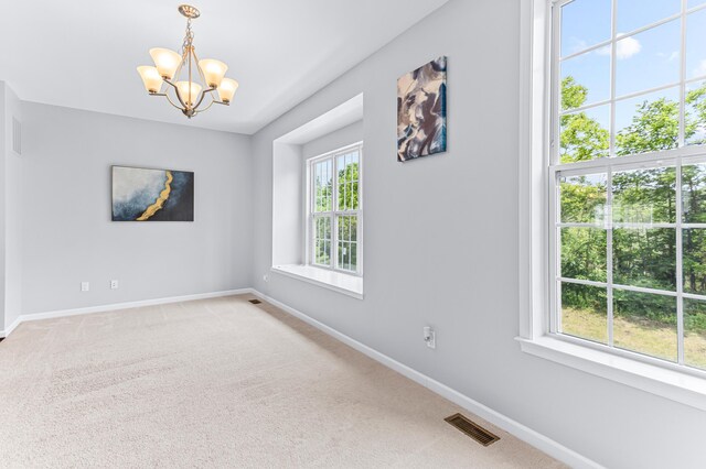empty room with a notable chandelier, baseboards, light colored carpet, and visible vents